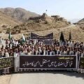 Peaceful protest by local residents in KP tribal districts against unrest, holding banners for permanent peace and civil rights, with mountains and a historic fort in the background - The Khyber Times