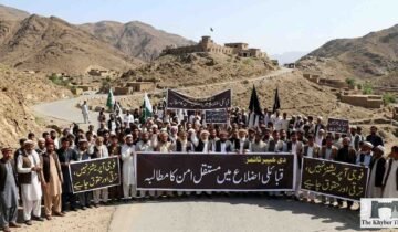 Peaceful protest by local residents in KP tribal districts against unrest, holding banners for permanent peace and civil rights, with mountains and a historic fort in the background - The Khyber Times