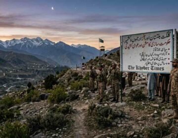 An informational sign detailing the political crisis, government formation, and public tension in Gilgit-Baltistan and Azad Kashmir, with soldiers and civilians in a mountain pass for The Khyber Times. دی خیبر ٹائمز کی خصوصی رپورٹ کے لیے گلگت بلتستان اور آزاد کشمیر میں حکومت سازی، سیاسی جوڑ توڑ اور عوامی کشیدگی کے مسائل کو ظاہر کرتا ہوا ایک معلوماتی بورڈ اور مقامی منظر۔