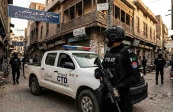 KP Police CTD personnel standing alert next to a police vehicle in Meena Bazar, Peshawar, for a Khyber Times news report.