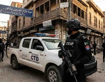 KP Police CTD personnel standing alert next to a police vehicle in Meena Bazar, Peshawar, for a Khyber Times news report.