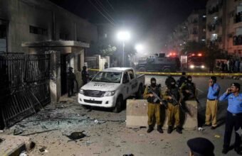 "Crime scene aftermath of the Gulistan-e-Jauhar Rangers attack in Karachi, showing damaged gate, destroyed vehicle, heavy security, and police presence."
