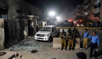 "Crime scene aftermath of the Gulistan-e-Jauhar Rangers attack in Karachi, showing damaged gate, destroyed vehicle, heavy security, and police presence."