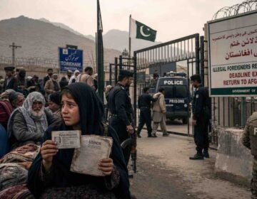 "Documentary photograph at the Torkham border dividing weary Afghan refugee families on the left from Pakistani security forces and a deportation notice on the right, representing the post-deadline repatriation and humanitarian crisis."
