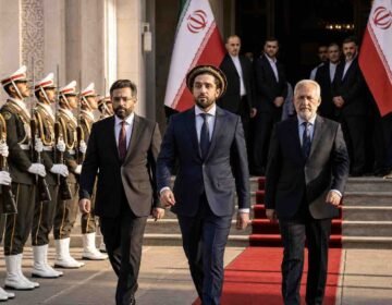 "Ahmad Massoud and the National Resistance Front (NRF) delegation walking on a red carpet at an official government reception in Tehran, flanked by Iranian honor guards."