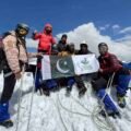 Nine climbers from Khyber Pakhtunkhwa celebrate after summiting the 6,050-meter Thalo Zom Peak, holding the Pakistani flag and the KP Culture & Tourism Authority flag.