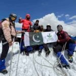Nine climbers from Khyber Pakhtunkhwa celebrate after summiting the 6,050-meter Thalo Zom Peak, holding the Pakistani flag and the KP Culture & Tourism Authority flag.