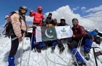 Nine climbers from Khyber Pakhtunkhwa celebrate after summiting the 6,050-meter Thalo Zom Peak, holding the Pakistani flag and the KP Culture & Tourism Authority flag.