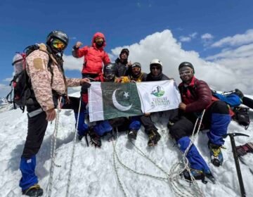 Nine climbers from Khyber Pakhtunkhwa celebrate after summiting the 6,050-meter Thalo Zom Peak, holding the Pakistani flag and the KP Culture & Tourism Authority flag.