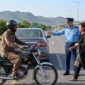 Alt Text: A PAF officer in uniform signaling a distressed woman to safety on an Islamabad highway with a motorcyclist nearby and Margalla Hills in the background.