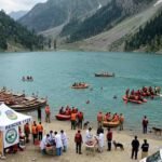 Rescue 1122 emergency response operation at an alpine lake in Swat Valley, showing an overturned tourist boat, rescue inflatable rafts, ambulances, and a medical tent on the shore.
