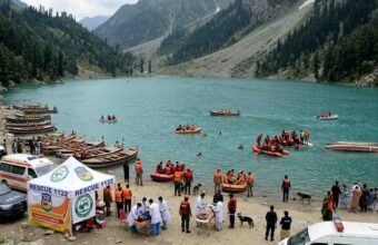 Rescue 1122 emergency response operation at an alpine lake in Swat Valley, showing an overturned tourist boat, rescue inflatable rafts, ambulances, and a medical tent on the shore.
