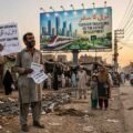 A poor Pakistani man holding a utility bill looks up ironically at a massive government billboard claiming economic development, showcasing the stark contrast of the debt crisis.