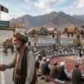 Pakistani and Afghan elders shaking hands at the border with a Grand Jirga meeting in the background representing peace and diplomacy.