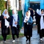 Four young Afghan schoolgirls in black uniforms and white headscarves walking together on a street in Kabul.