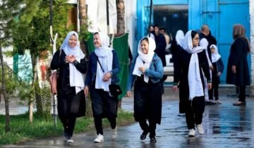 Four young Afghan schoolgirls in black uniforms and white headscarves walking together on a street in Kabul.