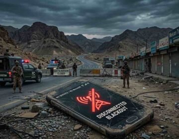 A smartphone with a glowing red 'No Service / Disconnected' blackout icon lying on a dusty road, flanked by security personnel patrolling a blocked mountain highway and closed market shops in Balochistan.