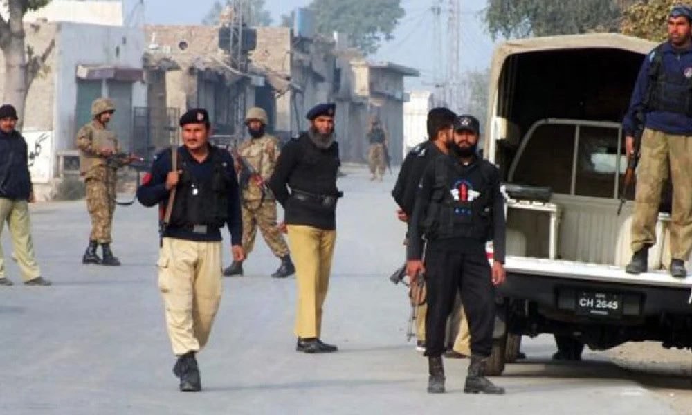 Pakistani security personnel from KP Police and Army standing on a dusty urban street in Peshawar, Khyber Pakhtunkhwa, next to a police vehicle with license plate CH 2645. Buildings with Urdu signs are visible.