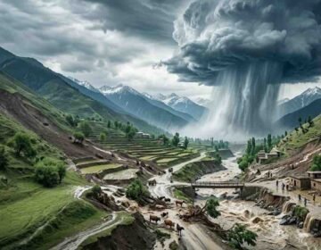 A dramatic aerial view of a severe cloudburst over mountainous terrain in Khyber Pakhtunkhwa, Pakistan, showing torrential rain triggering flash floods, soil erosion, and rural village destruction along a swollen river.