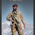 NRF field commander Haseeb Panjshiri standing on a mountain peak in military camouflage gear and a pakol hat holding a rifle against snow-capped Afghan mountains.