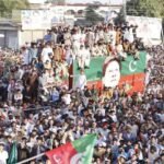 Primary Alt Text: Massive PTI power show rally with supporters holding party flags around a decorated container displaying Imran Khan's portrait.