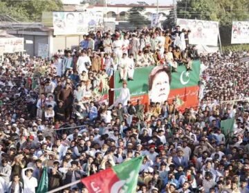 Primary Alt Text: Massive PTI power show rally with supporters holding party flags around a decorated container displaying Imran Khan's portrait.