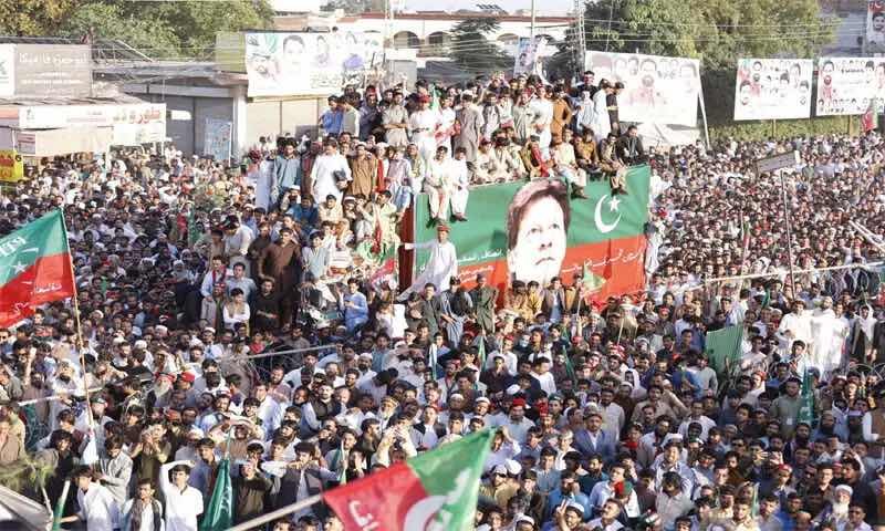 Primary Alt Text: Massive PTI power show rally with supporters holding party flags around a decorated container displaying Imran Khan's portrait.