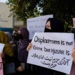 Afghan refugees hold protest signs outside the UNHCR office in Peshawar, urging protection and third-country resettlement.