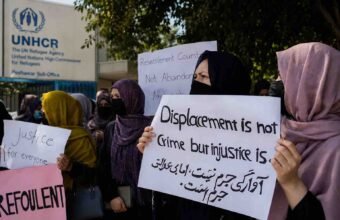 Afghan refugees hold protest signs outside the UNHCR office in Peshawar, urging protection and third-country resettlement.