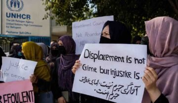 Afghan refugees hold protest signs outside the UNHCR office in Peshawar, urging protection and third-country resettlement.