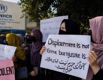 Afghan refugees hold protest signs outside the UNHCR office in Peshawar, urging protection and third-country resettlement.