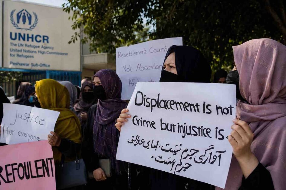 Afghan refugees hold protest signs outside the UNHCR office in Peshawar, urging protection and third-country resettlement.