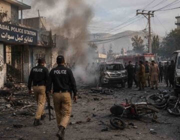 Police and rescue teams respond after a suicide attack at Kabal Police Station in Swat, with smoke, damaged vehicles, and debris visible.