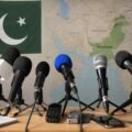 Microphones in a press briefing setup with the Pakistan flag and a map of Pakistan in the background