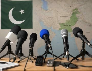 Microphones in a press briefing setup with the Pakistan flag and a map of Pakistan in the background