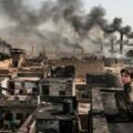 A young child sitting on a dusty rooftop overlooking a semi-urban landscape in Bara and Peshawar, with industrial brick kilns emitting thick black smoke into the hazy sky.