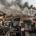 A young child sitting on a dusty rooftop overlooking a semi-urban landscape in Bara and Peshawar, with industrial brick kilns emitting thick black smoke into the hazy sky.
