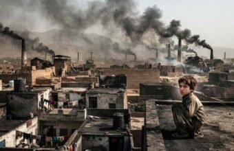 A young child sitting on a dusty rooftop overlooking a semi-urban landscape in Bara and Peshawar, with industrial brick kilns emitting thick black smoke into the hazy sky.