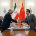 Iranian Parliament Speaker Mohammad Bagher Ghalibaf shaking hands with a Chinese official in front of the Iranian and Chinese flags.