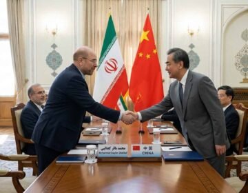 Iranian Parliament Speaker Mohammad Bagher Ghalibaf shaking hands with a Chinese official in front of the Iranian and Chinese flags.