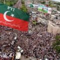 Alt Text: Aerial view of a massive Pakistan Tehreek-e-Insaf (PTI) protest rally crowd with a prominent red and green PTI flag in the foreground.