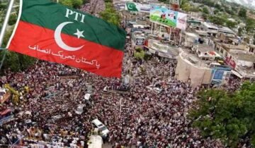 Alt Text: Aerial view of a massive Pakistan Tehreek-e-Insaf (PTI) protest rally crowd with a prominent red and green PTI flag in the foreground.