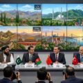 Wide photograph of a multilateral diplomatic press conference featuring Afghan, Pakistani, Chinese, and Turkish officials. Numerous press photographers are in the foreground, and a large multi-panel video screen in the background shows illustrative scenes of Kabul, Islamabad, Beijing, and Istanbul.