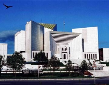 English: Front exterior view of the white marble Supreme Court of Pakistan building in Islamabad under a deep blue sky with a bird flying in the upper-left corner.