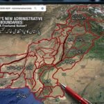 A close-up photograph of a large monitor displaying a satellite map of Pakistan, altered with a complex overlay of thick red lines creating a hypothetical subdivision of the country. At the top of the map, text in English reads: "PAKISTAN'S NEW ADMINISTRATIVE BOUNDARIES: A Fractured Nation?" Below it, Urdu text says: "پاکستان کا نیا انتظامی خاکہ: تقسیم در تقسیم؟" (translated as "Pakistan's New Administrative Plan: Division within Division?"). Numerous Urdu labels partition the map into smaller regions, including "جنوبی پنجاب" (South Punjab), "سرائیکستان" (Saraikistan), "پوٹوہار" (Pothohar), "مکران" (Makran), and "کراچی ریجن" (Karachi Region). Labels for adjacent territories like "INDIA", "AFGHANISTAN", "IRAN", "BALOMISTAN", "KARTAN", and "BHOJO" are also visible. A red pen tip is shown in the foreground near the bottom-center, poised near where "TANDO" (partially obscured) is written. The user interface mimics Google Maps, with a search bar and map controls. The background is a blurred view of multiple screens in a newsroom or control room.