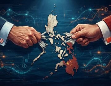A stylized, digital illustration shows a physical map of the Philippines archipelago in the center, being pulled apart by two hands. The hand on the left wears a suit cuff with a US flag pin, and the hand on the right wears a suit cuff with a Chinese flag pin. Glowing blue and red lines and data interfaces emanate from the map and the hands, suggesting digital warfare and geopolitical influence.