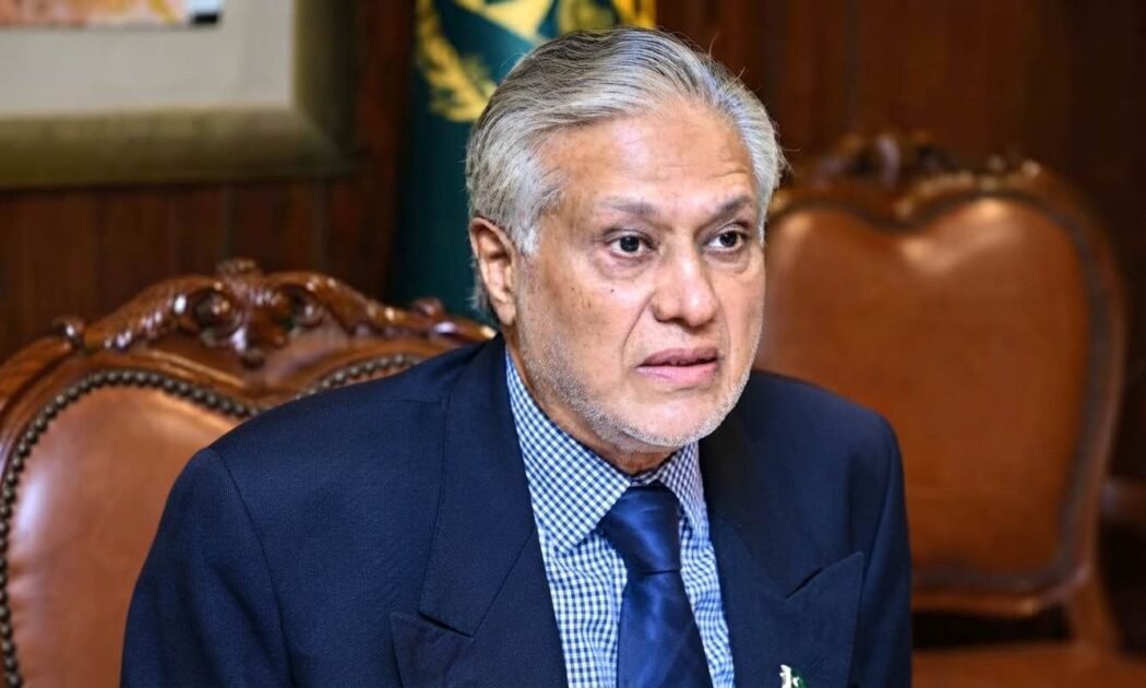 Accessibility for visually impaired users and search engines. Describes what is actually visible in the image. Portrait of Pakistani politician Ishaq Dar, with grey hair and beard, wearing a navy suit and checkered shirt, looking intently towards the right while seated in a traditional wooden armchair.