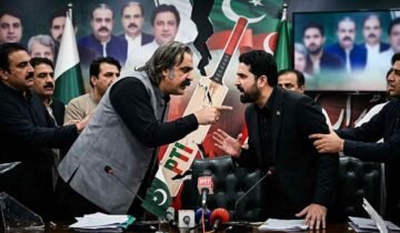 Tensions erupt into a direct confrontation between two men during a Pakistani political meeting, with other attendees attempting to keep them apart amidst a backdrop of political portraits and a fractured party symbol. Alt Text: A phot
