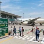 A digital illustration of Islamabad International Airport terminal showing a PIA aircraft on the tarmac, passengers walking, and a green directional sign board detailing the Pak-Afghan transit agreement to the Gulf.