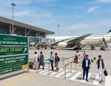 A digital illustration of Islamabad International Airport terminal showing a PIA aircraft on the tarmac, passengers walking, and a green directional sign board detailing the Pak-Afghan transit agreement to the Gulf.